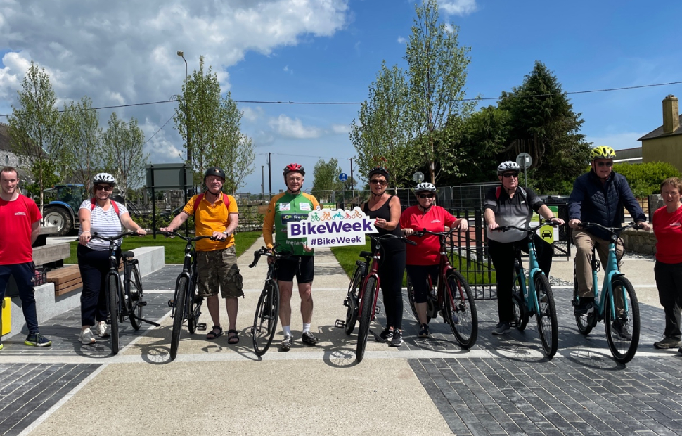 group of bikers, both men and women, holding up bike week card and smiling to the camera